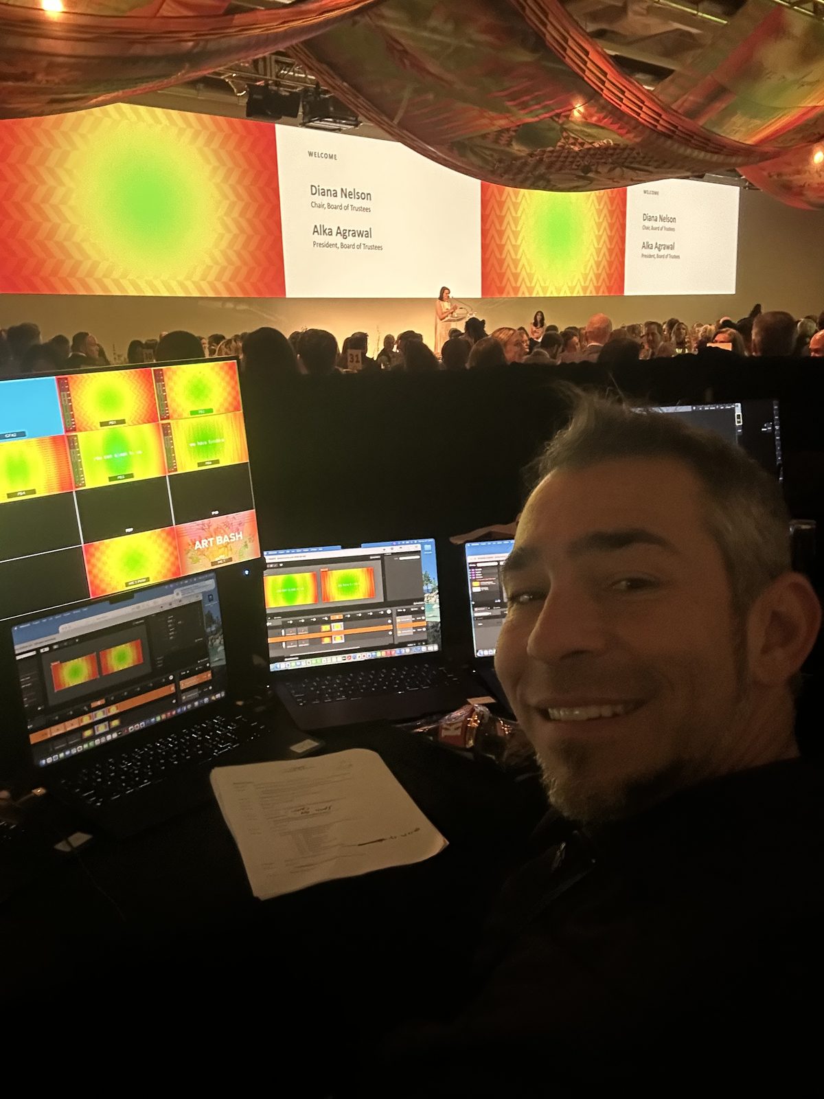 Greg Castellanos running graphics and playback from the production desk at a live gala, with the stage and audience beyond.